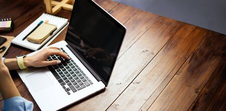 Mockup image of a woman using laptop with blank screen on wooden table. Female writer keyboarding on computer while working on her new articleの写真素材