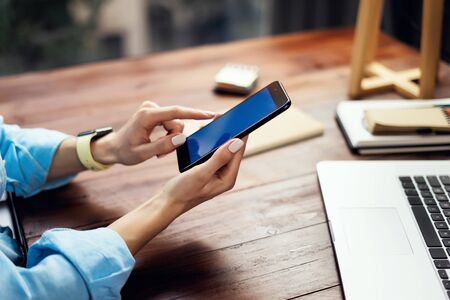 Mockup image of a woman using smartphone with blank screen on wooden table. Close up photo of female...