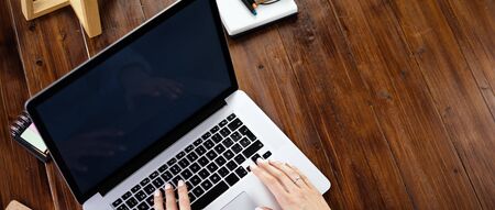 Mockup image of a woman using laptop with blank screen on wooden table. Female writer keyboarding on computer while working on her new articleの写真素材