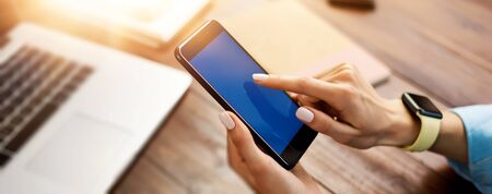 Mockup image of a woman using smartphone with blank screen on wooden table. Close up photo of female hands with mobile phoneの写真素材