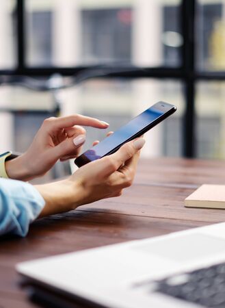 Woman pointing on smartphone screen, chatting in social networks, meeting website, searching internet, sending sms, using text messenger or online banking. Close up of female hands with mobile phoneの写真素材