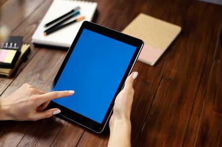 Mockup image of a woman using digital tablet with blank screen on wooden table. Close up photo of female hands holding device uprightの写真素材