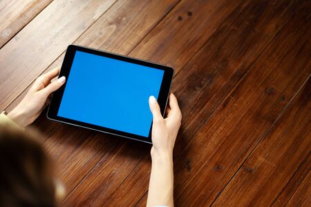 Mockup image of a digital tablet with blank screen on wooden table. Close up photo of female hands holding device horizontallyの写真素材