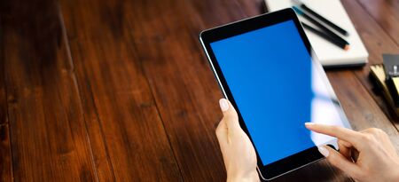 Mockup image of a woman using digital tablet with blank screen on wooden table. Close up photo of female hands holding device uprightの写真素材