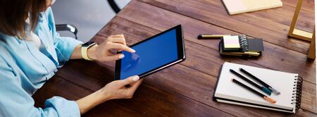 Mockup image of a woman using digital tablet with blank screen on wooden table. Close up photo of female hands holding device uprightの写真素材
