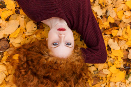 cute red-haired girl lying on yellow leaves.