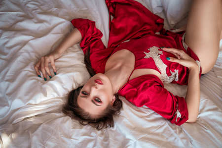 sexy woman lying on the bed in a red negligee, bright beautiful make-up.の写真素材