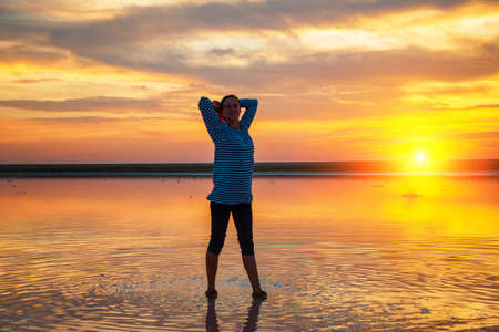 silhouette of a woman on the water at sunset, beautiful sunset sky with clouds, tourism concept.の写真素材