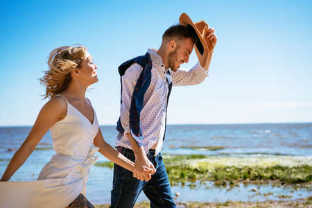 a young couple in love walks on the beach against the background of the sea, a blonde girl with a...