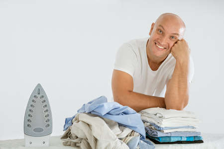 A man on a white background with an Ironing Board, there is an iron and there are ironed things and not ironed.の写真素材