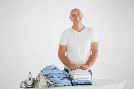 A man on a white background with an Ironing Board, there is an iron and there are ironed things and not ironed.の写真素材