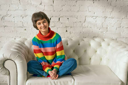 Cheerful woman in a rainbow sweater sitting on the sofa, concept.の写真素材