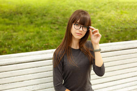 Portrait of a cute girl with glasses, sitting on a bench on the street in the Park.の写真素材