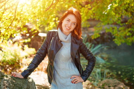 Happy woman in a leather jacket in a Park near a tree smiling.