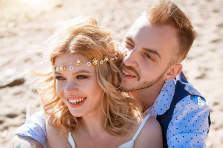 Portrait of a young couple, blonde girl and light-haired bearded guy, sitting on the beach. Love...