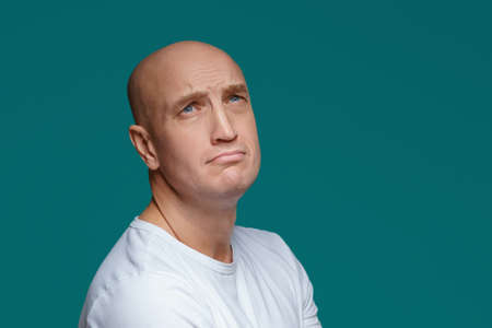 Portrait of a bald adult man with a sad expression in a white t shirt on a blue background.の写真素材
