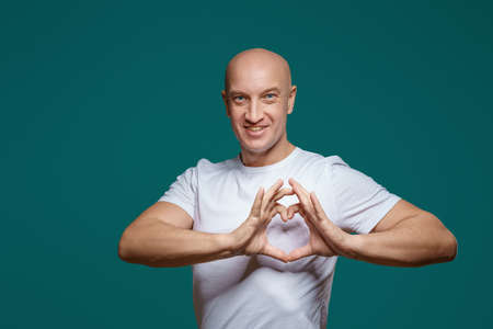 Portrait of a bald man smiling and holding hands in the shape of a heart, on a blue background . The...