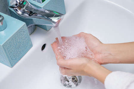 Woman washes her hand in the bathroom sink, without a face.
