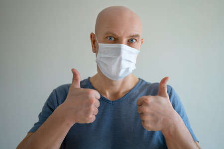 Portrait of a bald man in a medical mask, shows a hand gesture like a finger up.の写真素材