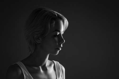 Female portrait close-up looks away, black and white photo dark.