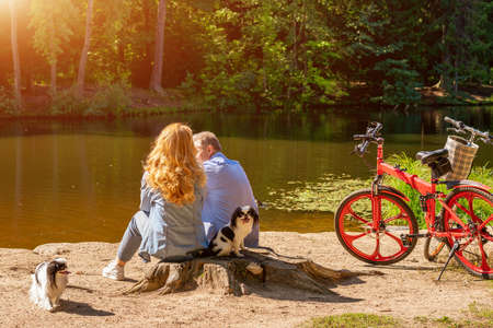Mature couple by the lake with a dog and a Bicycle sitting in the sun.の写真素材