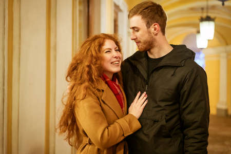 A happy couple stands in an embrace on the street in the evening in the festive lights.