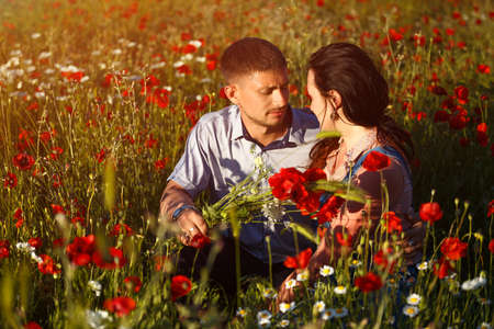 A romantic couple in a poppy field sitting in an embrace on a Sunny day.の写真素材