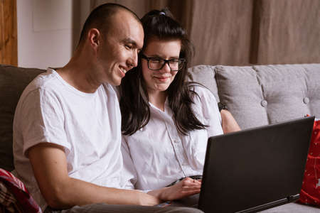 A married couple sitting at home on the sofa with a laptop order goods online.