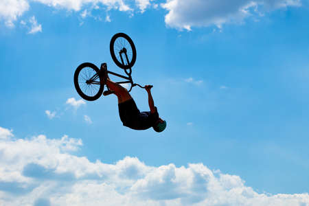 Silhouette of a man jumping on a Bicycle against a blue sky with white clouds. Guy performs tricks...