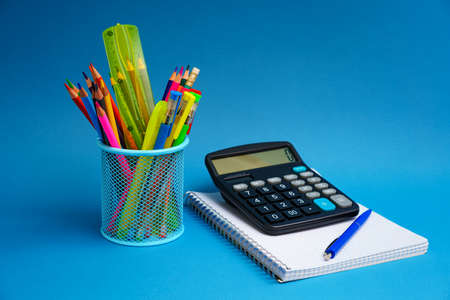 A holder with pens and pencils and a notebook with a calculator on a blue background. Back to school...