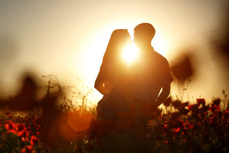 A happy couple silhouette in a poppy field in the rays of the setting sun hugging . The concept of romantic relationshipsの写真素材