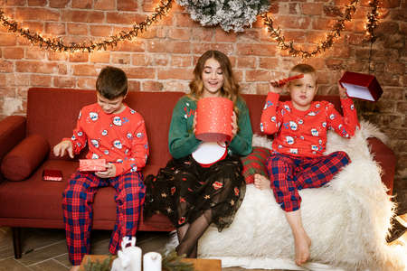 Two brothers and sister open gifts sitting on the sofa, happy faces, festive new year atmosphere.の写真素材