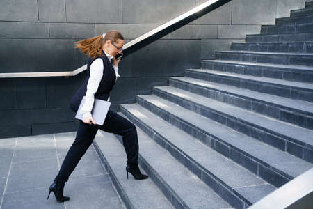 A business woman walks up the steps holding a tablet in her hand and talking on the phone. Conceptual horizontal photoの写真素材