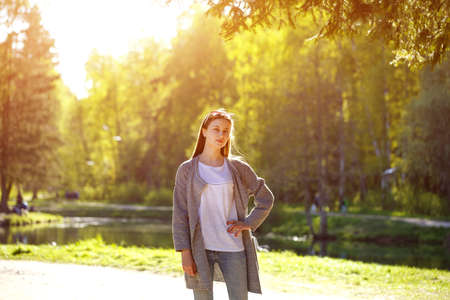 A young woman poses in the sun in the Park at the lake against the background of trees.の写真素材