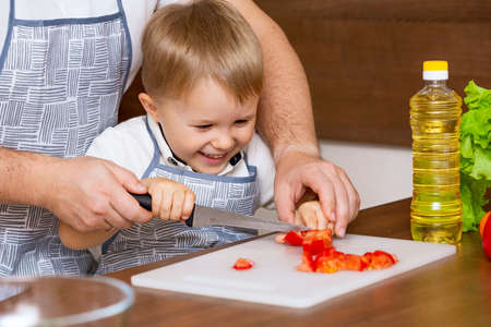 A happy father and a young son prepare a salad in the kitchen with vegetables. My dad teaches me how to cut tomatoes on a blackboard. Concept of diet foodの写真素材