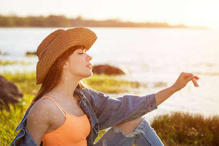Portrait of a young woman with a cowboy hat on the beach sitting on the beach in the rays of the...