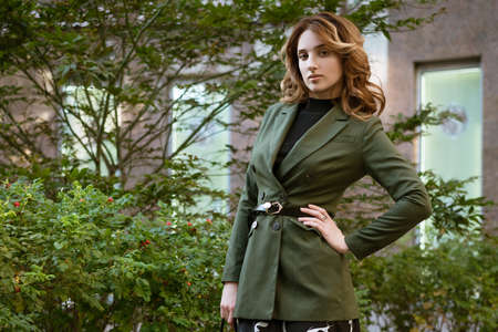 A beautiful young woman in stylish clothes with hair and makeup poses for the camera on the street in the daytime.の写真素材