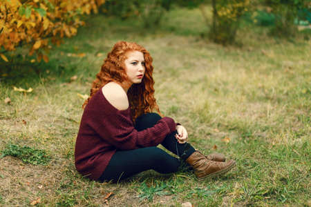 portrait of a beautiful young red-haired woman on the background of autumn landscape