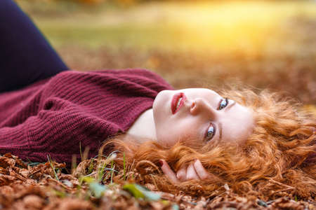 red-haired girl lies in the fallen yellow foliageの写真素材