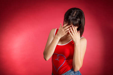 a young woman covered her face with her hands , on a red background