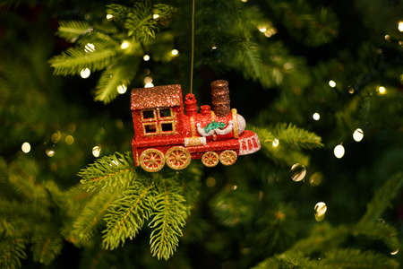 red shiny glass toy locomotive hanging on Christmas tree with garland , Christmas decoration