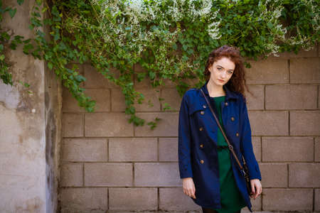 Portrait of a beautiful young woman with red hair and freckles on a background of wall and greenery