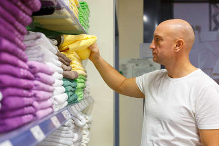 Bald man chooses towels on shelves in a store, shopping concept