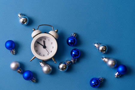 White alarm clock on a blue background with Christmas balls. The concept of the festive decorationsの写真素材