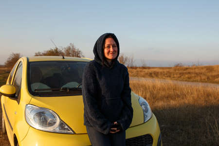 Woman standing outdoors in a yellow car on a background of blue sky, concept of traveling aloneの写真素材