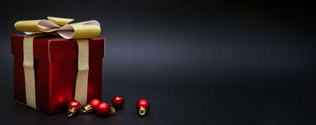 Red gift box with balls for decorating a Christmas tree on a black background. Holiday postcard
