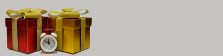 Gift red and gold boxes and white alarm clock on light background