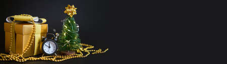 gift box with a gold bow. White alarm clock and a small Christmas tree on a black background.の写真素材