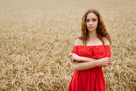 Beautiful happy young woman with curly hair in a red dress posing in a wheat fieldの写真素材