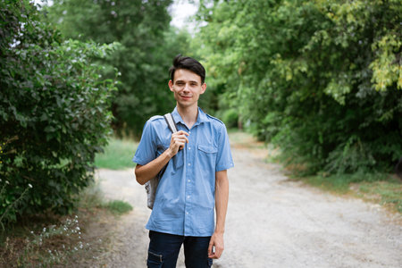 Young cheerful guy student stands in a blue shirt with a backpack on the road
